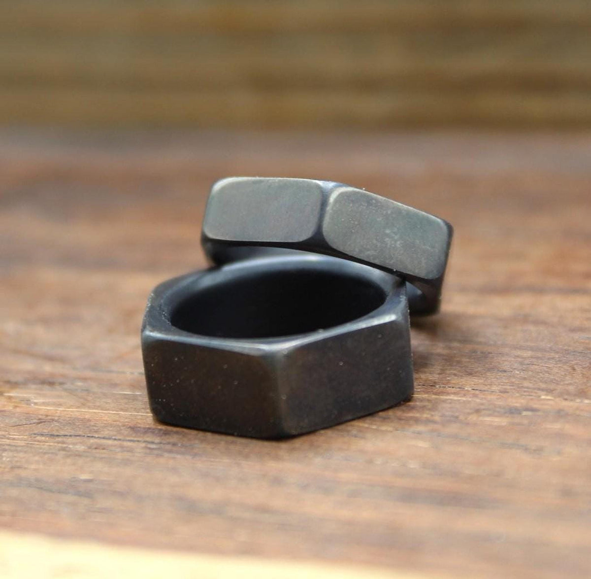One dark gray hexagonal ring resting on top of another dark gray hexagonal ring, viewed from a slight angle.