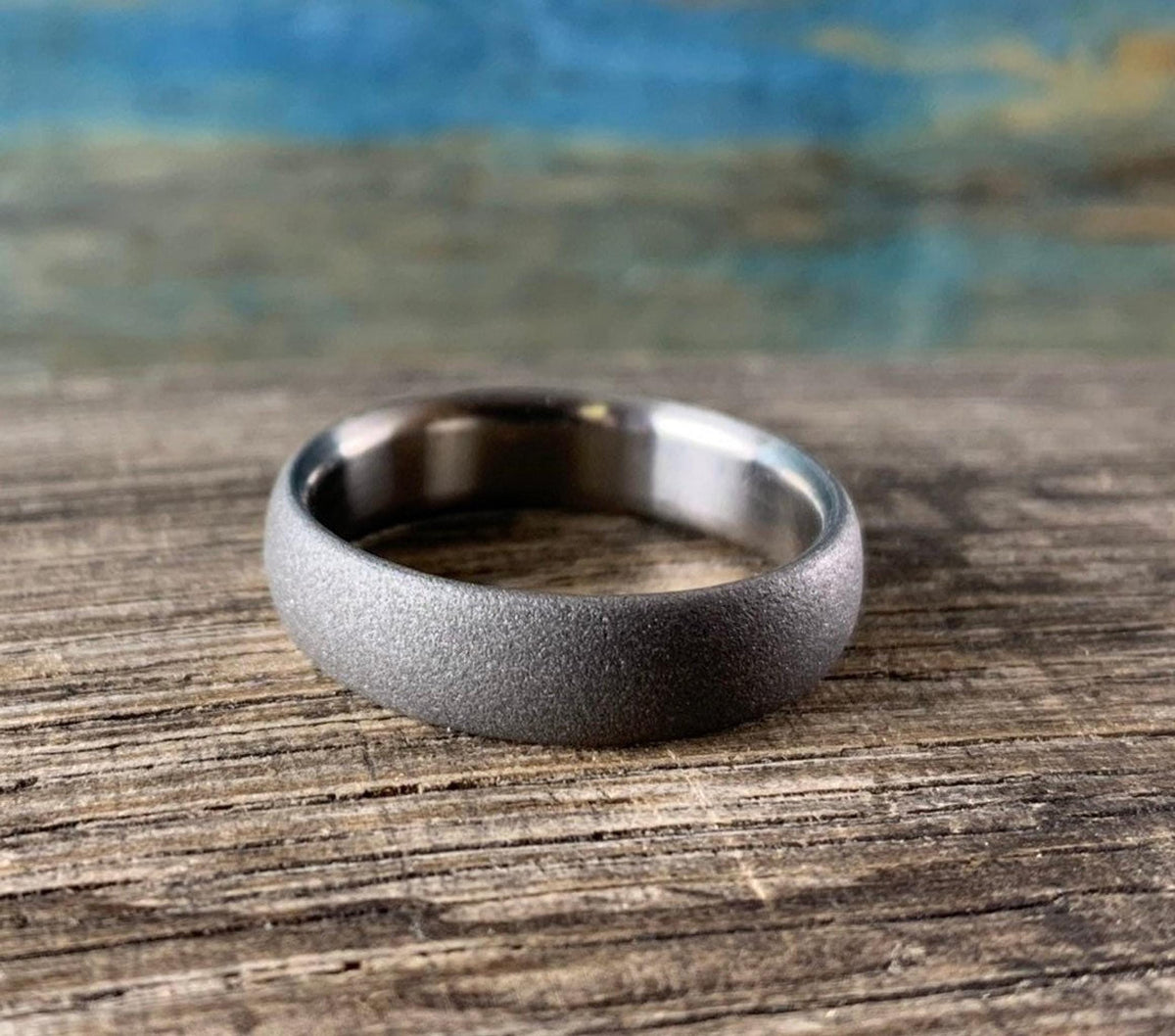 Matte sandblasted titanium wedding band displayed on rustic weathered wood