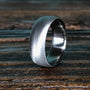A silver-colored ring with a brushed, textured exterior and a smooth, polished interior, resting on a dark wooden surface.