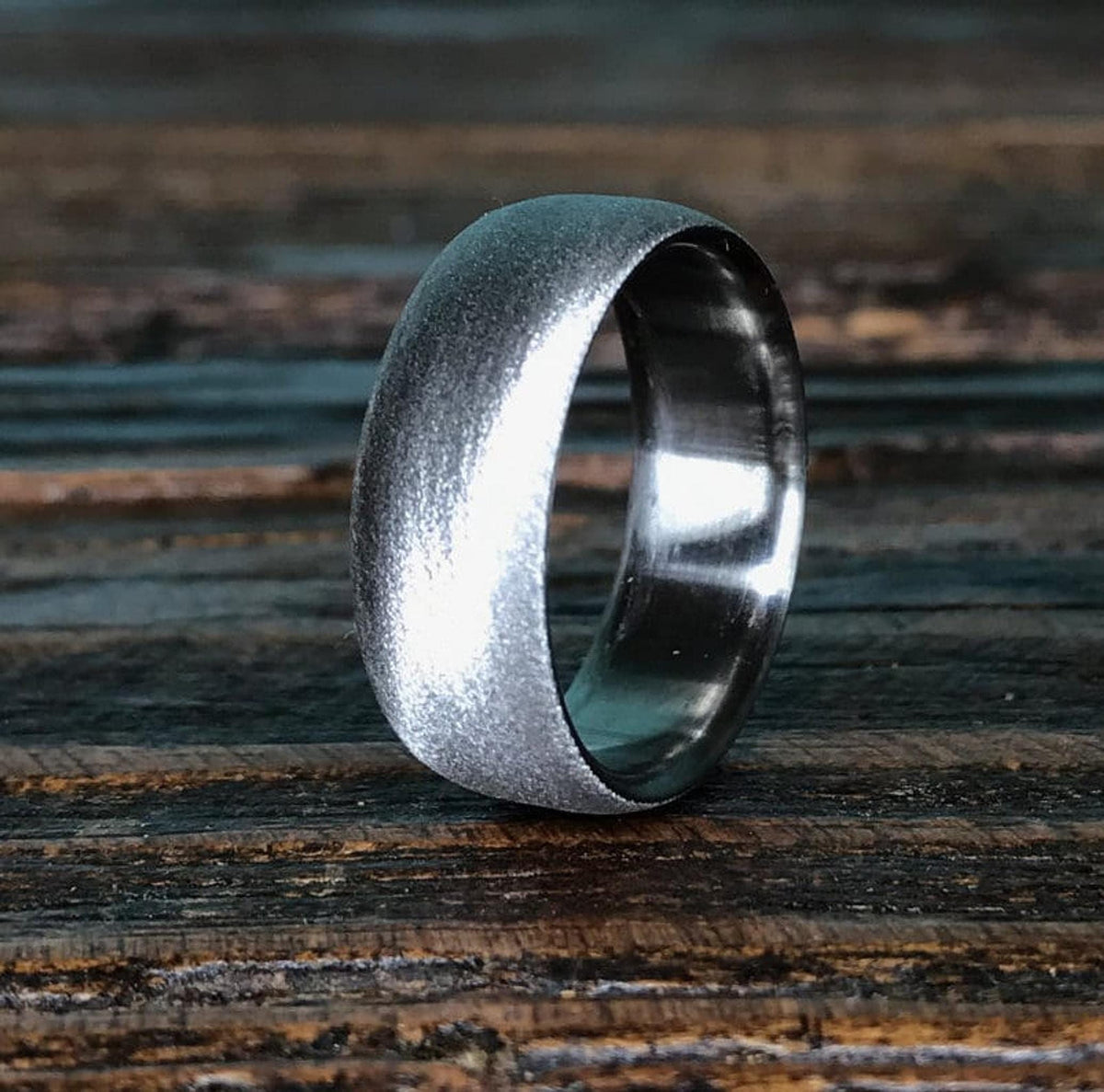 A silver-colored ring with a brushed, textured exterior and a smooth, polished interior, resting on a dark wooden surface.