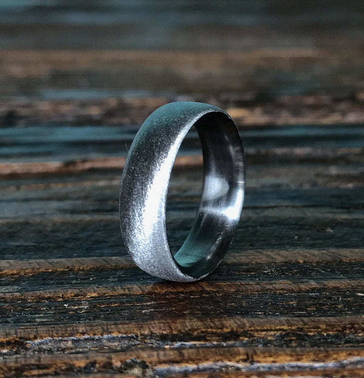 A silver-colored ring with a textured exterior and a smooth interior, standing upright on a dark wooden surface.
