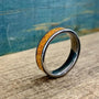 A silver-toned ring with an orange glittery inlay, angled on a wooden surface with a blue background.