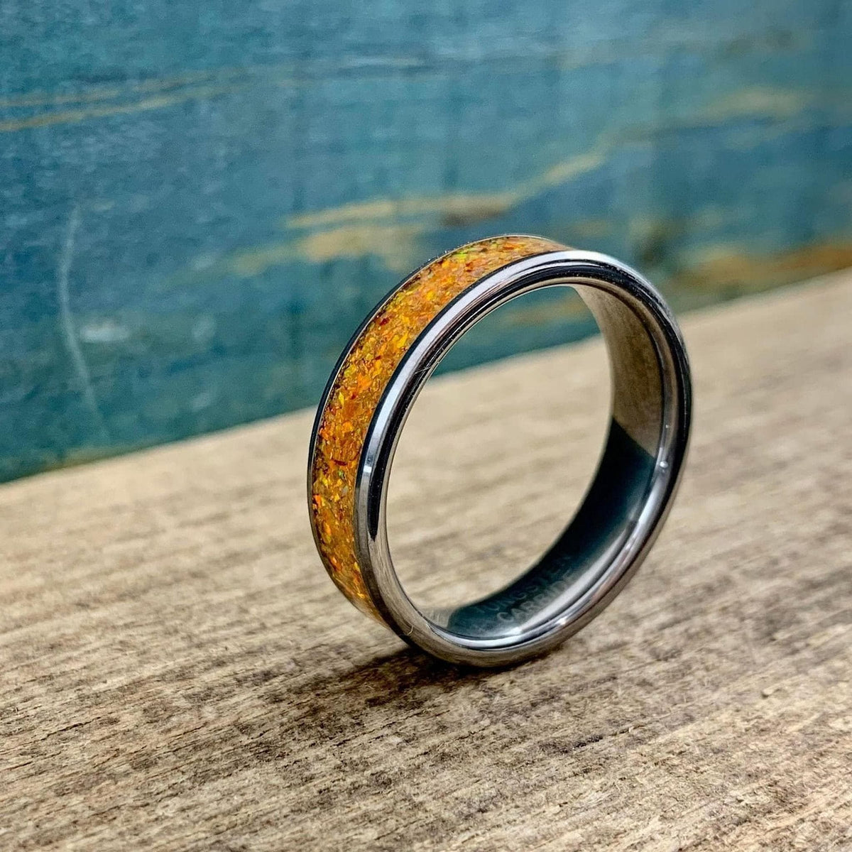 A silver-toned ring with an orange glittery inlay, angled on a wooden surface with a blue background.