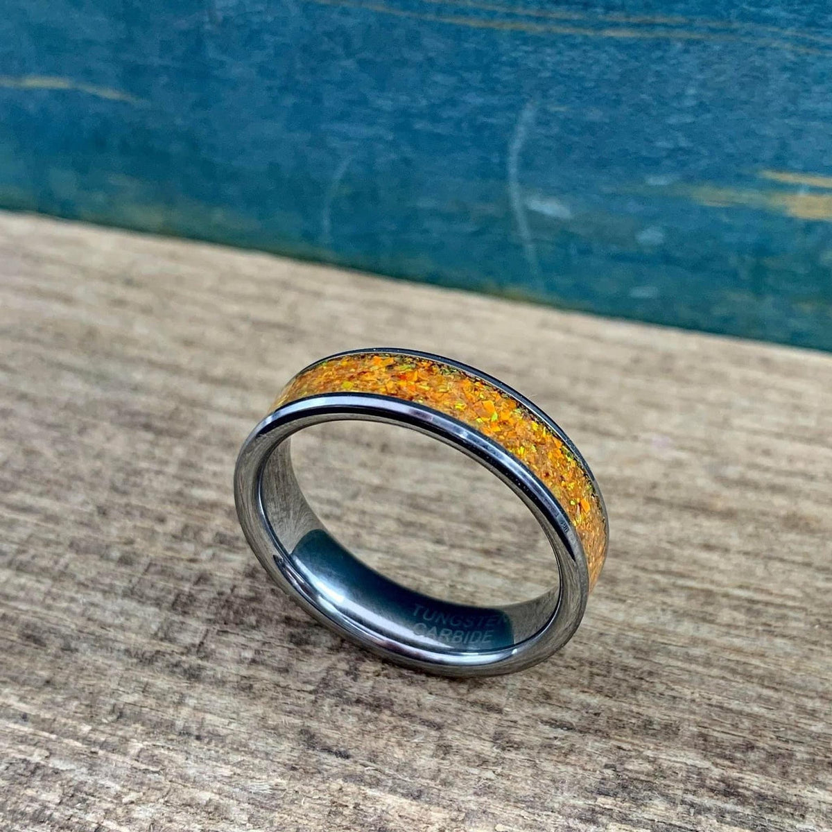 A silver-toned ring with an orange glittery inlay, angled slightly to the left on a wooden surface with a blue background.