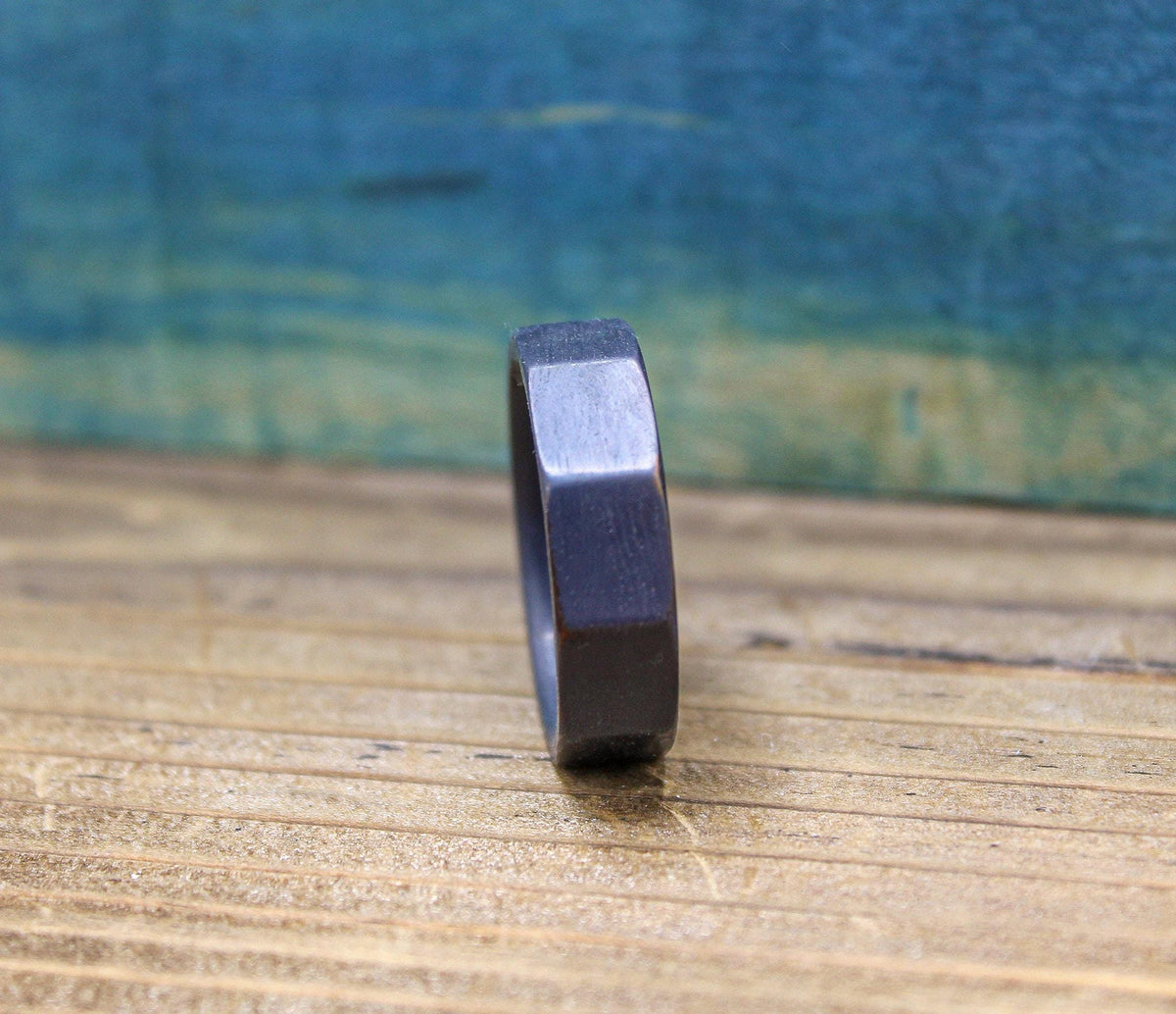 A dark gray, ten-sided ring stands upright on a light brown wooden surface, with a blurred blue background.