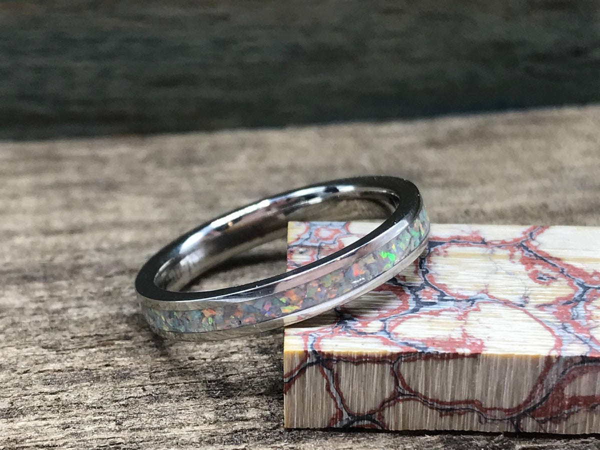 A silver ring with a white opal inlay rests on a wooden surface, with a block of red and white patterned wood to its right.