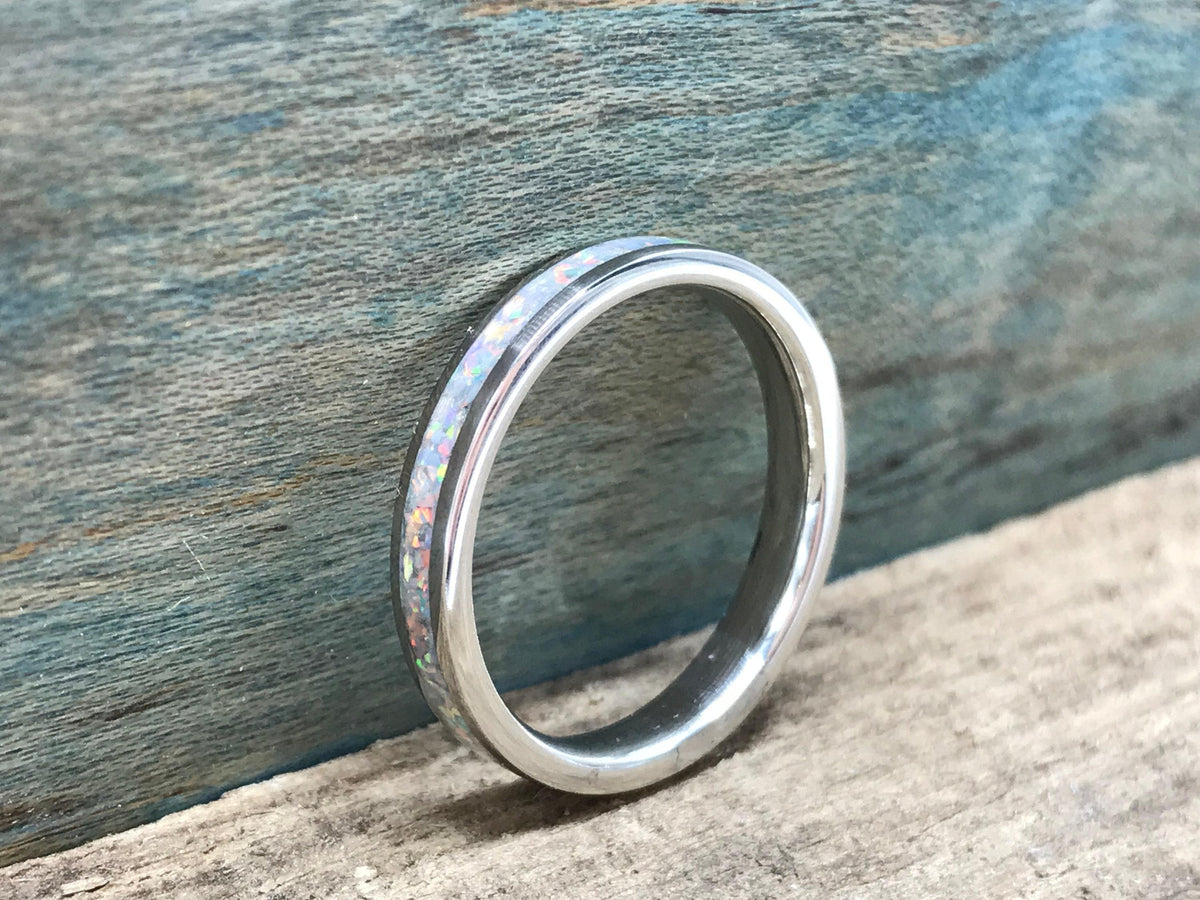A silver ring with a white opal inlay is positioned on a wooden surface, with a blue-painted wood background.