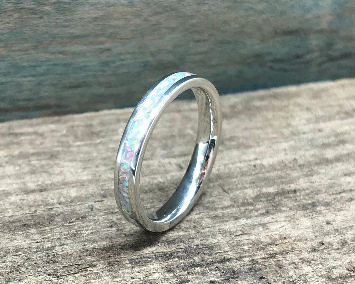 A silver ring with a white opal inlay is shown from a slightly elevated angle on a light wooden surface.