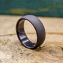 A dark gray, sandblasted ring with a smooth interior, angled on a light wooden surface.