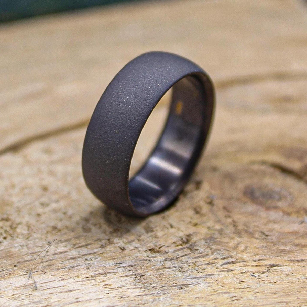 A dark gray, sandblasted ring with a smooth interior, slightly angled on a light wooden surface.