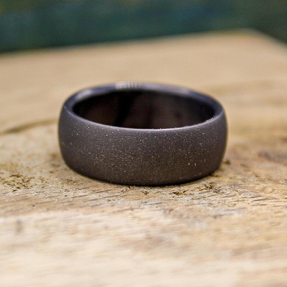 A dark gray, sandblasted ring with a smooth interior, viewed from the top on a light wooden surface.