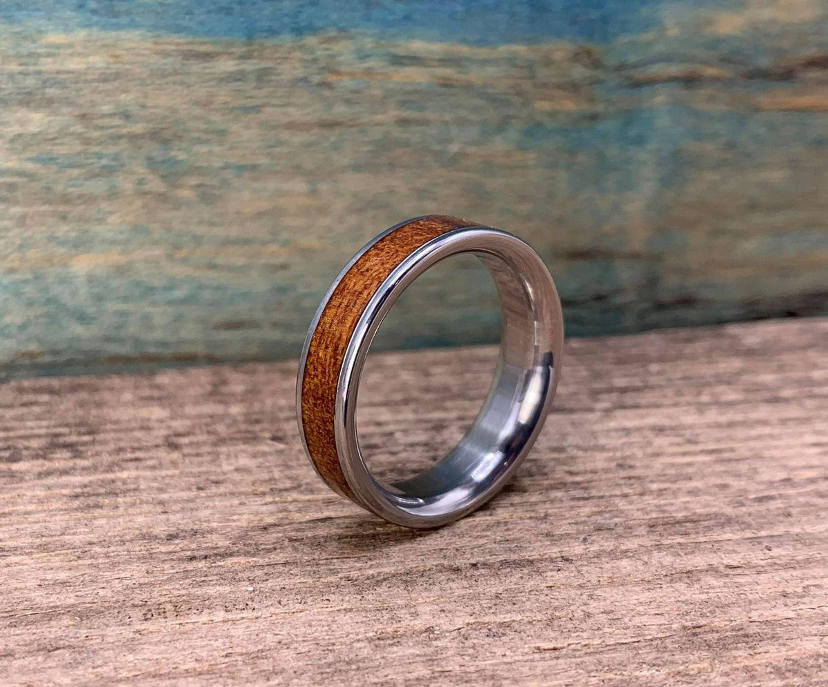 A silver-colored ring with a brown wood inlay is angled on a wooden surface, with a blue-green background.