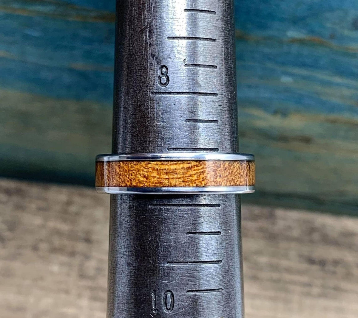 A silver-colored ring with a brown wood inlay is placed on a metal ring sizer, showing size 8.