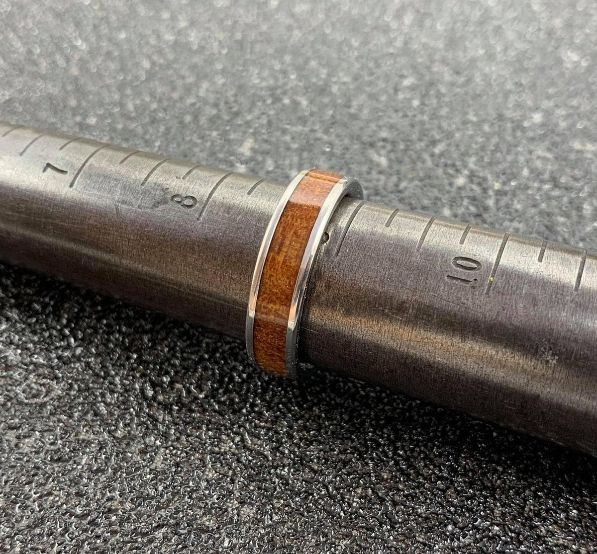 A silver-colored ring with a brown wood inlay is placed on a metal ring sizer, showing sizes 7 and 8.