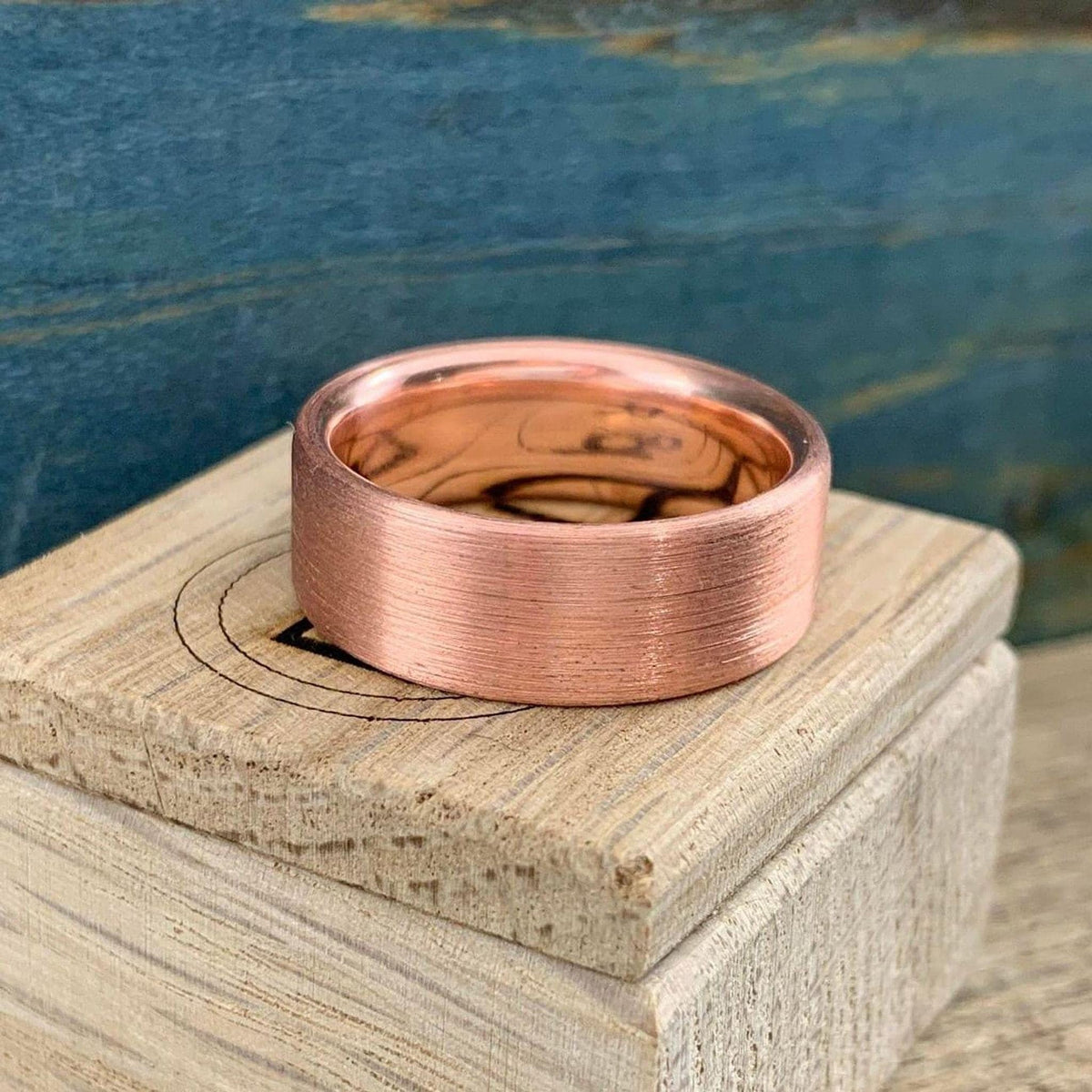 A brushed copper ring with a rounded interior, resting on a light wooden block with a circular engraving.