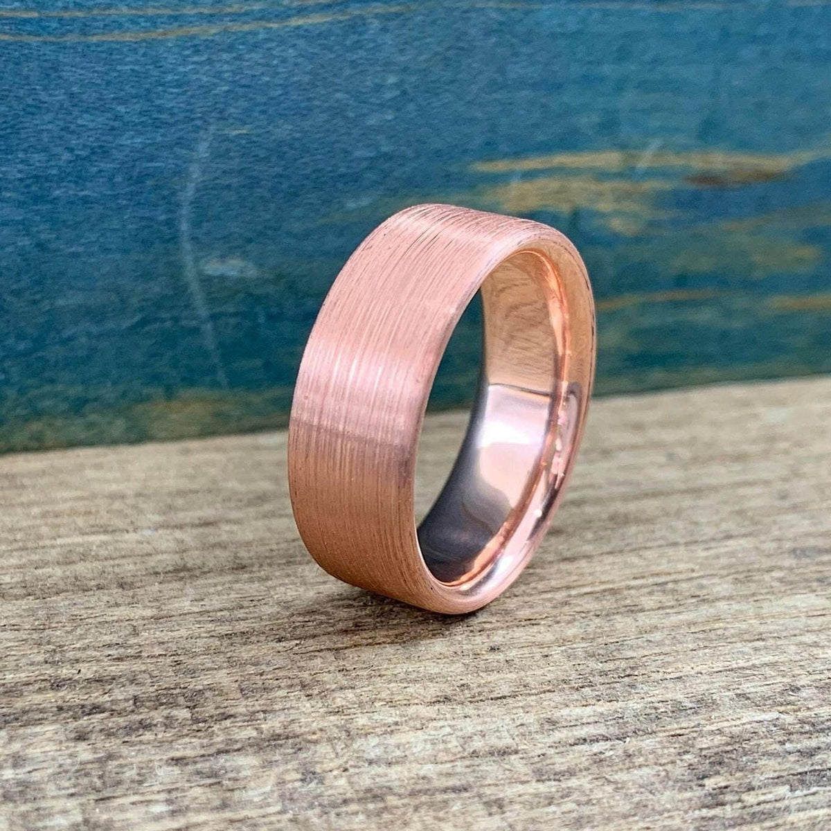 A brushed copper ring with a rounded interior, angled on a wooden surface with a blue background.