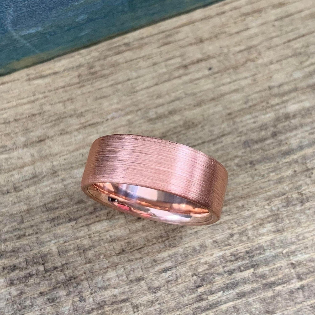 A brushed copper ring with a rounded interior, shown from a low angle on a wooden surface.