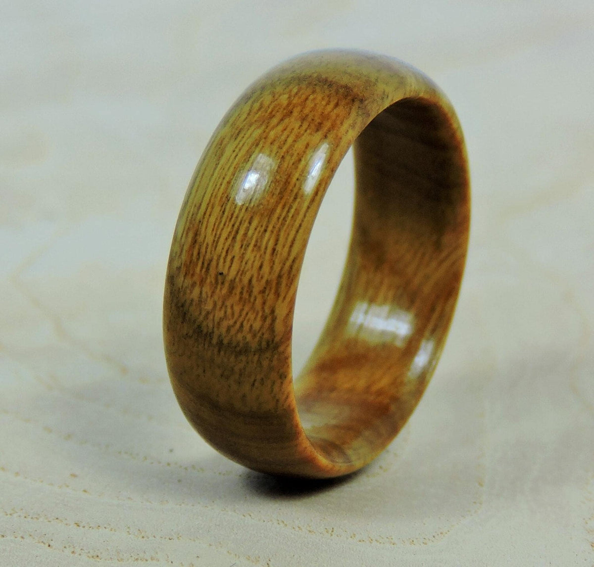 A smooth, polished, light brown wooden ring with fine vertical grain lines stands upright on a light wooden surface.