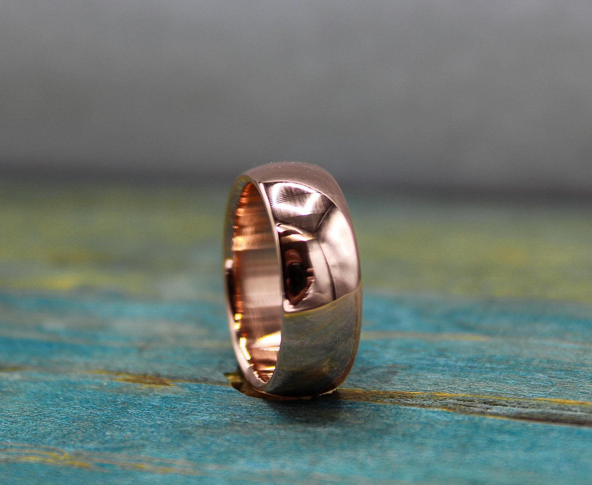 A polished, rose gold-toned ring with a domed exterior and a flat interior, resting on a distressed blue-green wooden surface.