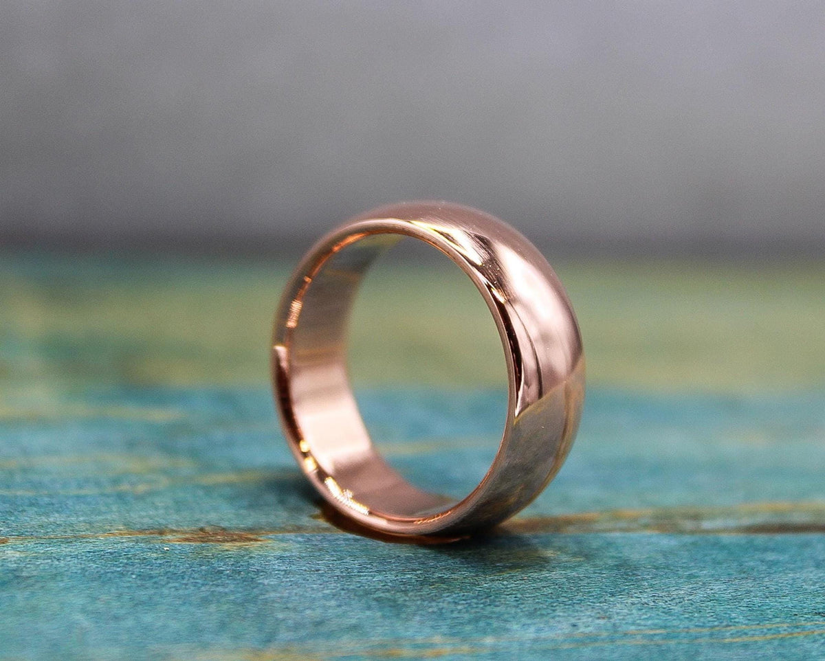 A polished, rose gold-toned ring with a domed exterior and a flat interior, resting on a distressed blue-green wooden surface.