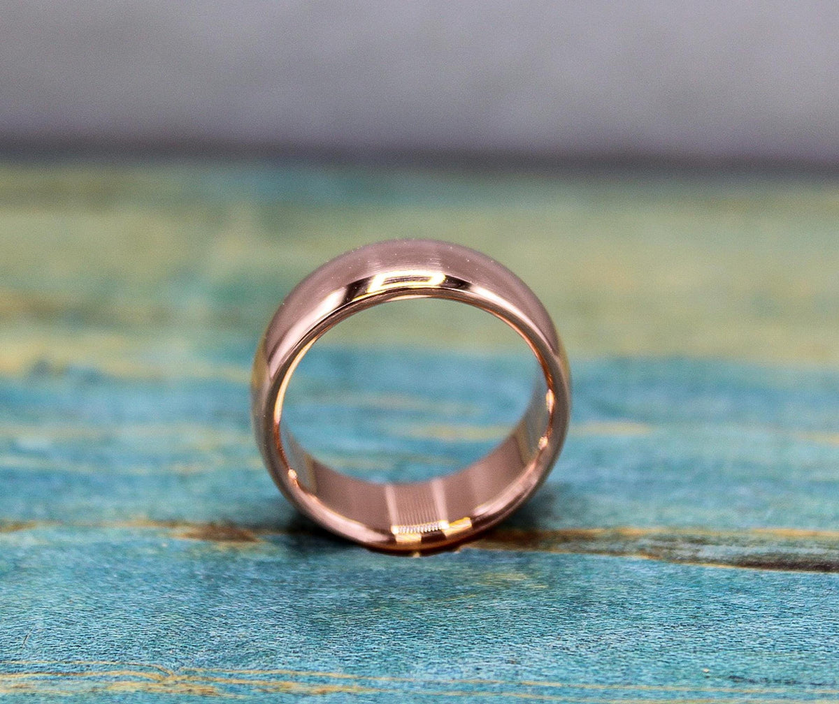 A rose gold-toned ring with a brushed finish on the outer band and a smooth, reflective inner band, resting on a distressed blue-green wooden surface.