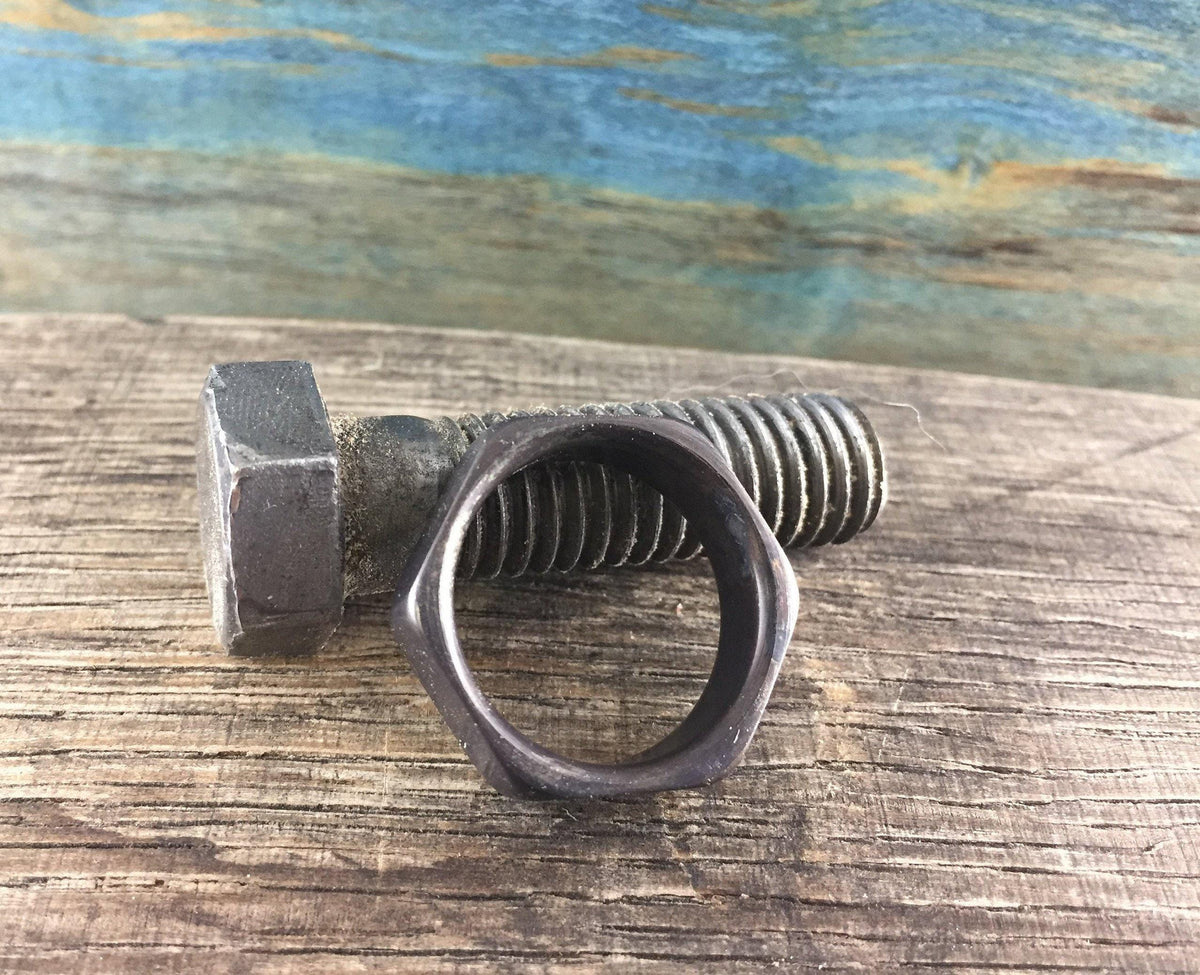 A dark hexagonal ring is placed next to a large, rusty metal bolt on a wooden surface.