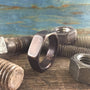 A dark hexagonal ring rests on a wooden surface surrounded by three large, rusty metal nuts and bolts.