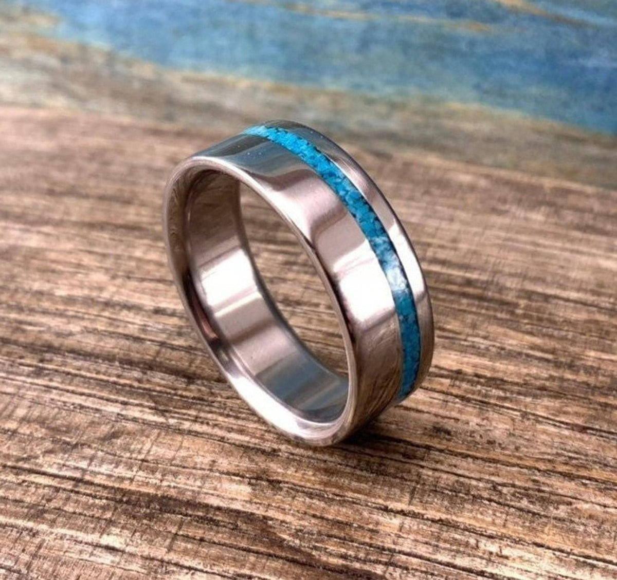 A silver-colored ring with a turquoise inlay, positioned on a wooden surface with a blue background.