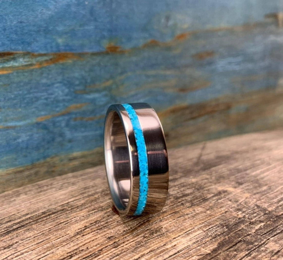 A silver-colored ring with a turquoise inlay, viewed from a slight angle on a wooden surface.