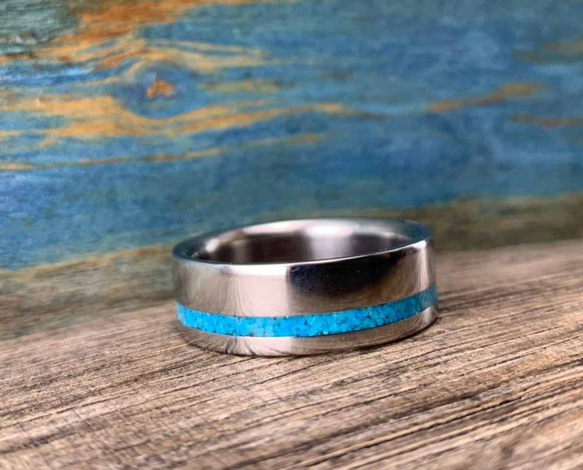 A silver-colored ring with a turquoise inlay, shown from the side on a wooden surface.