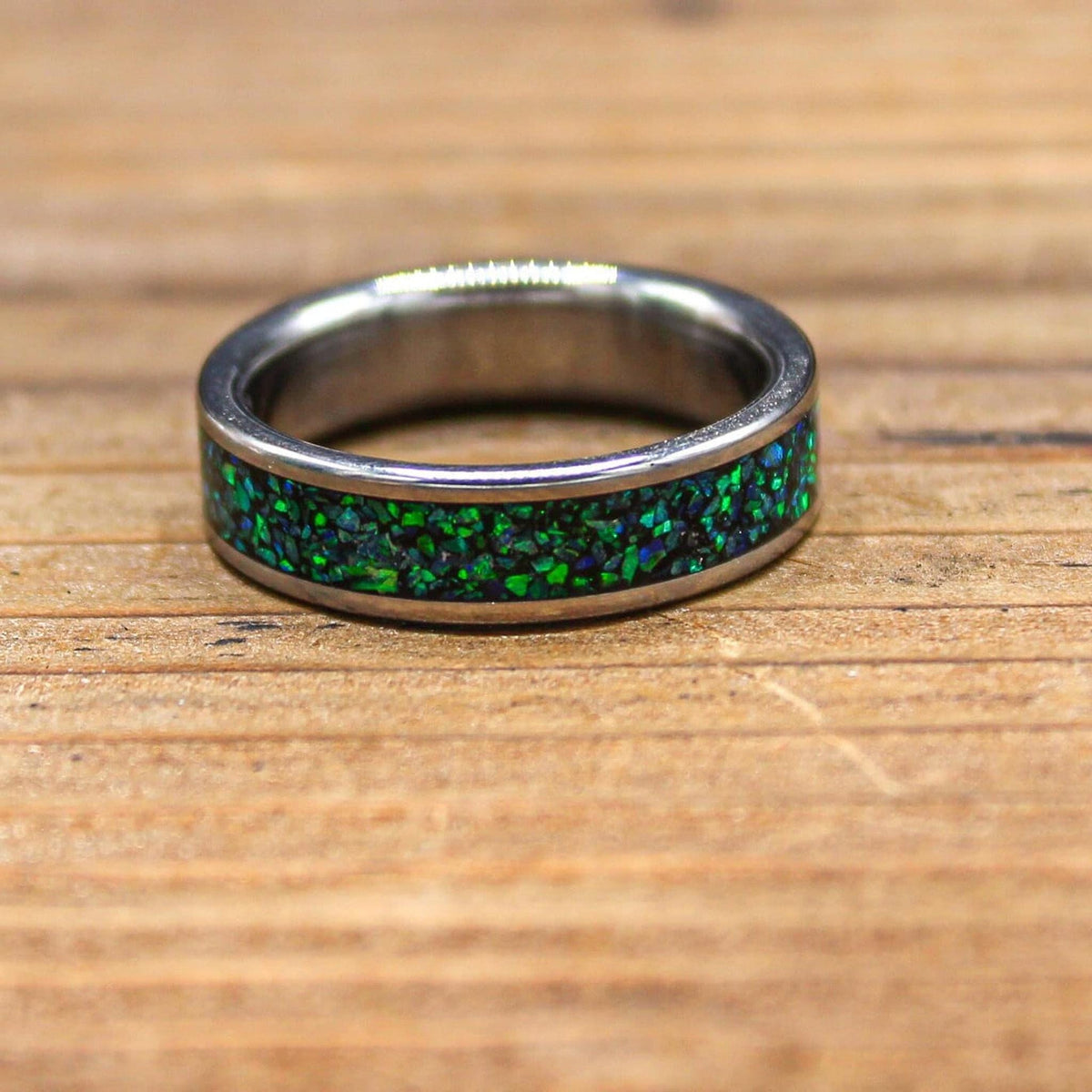 A silver-colored ring with a green and blue speckled inlay lies flat on a wooden surface.