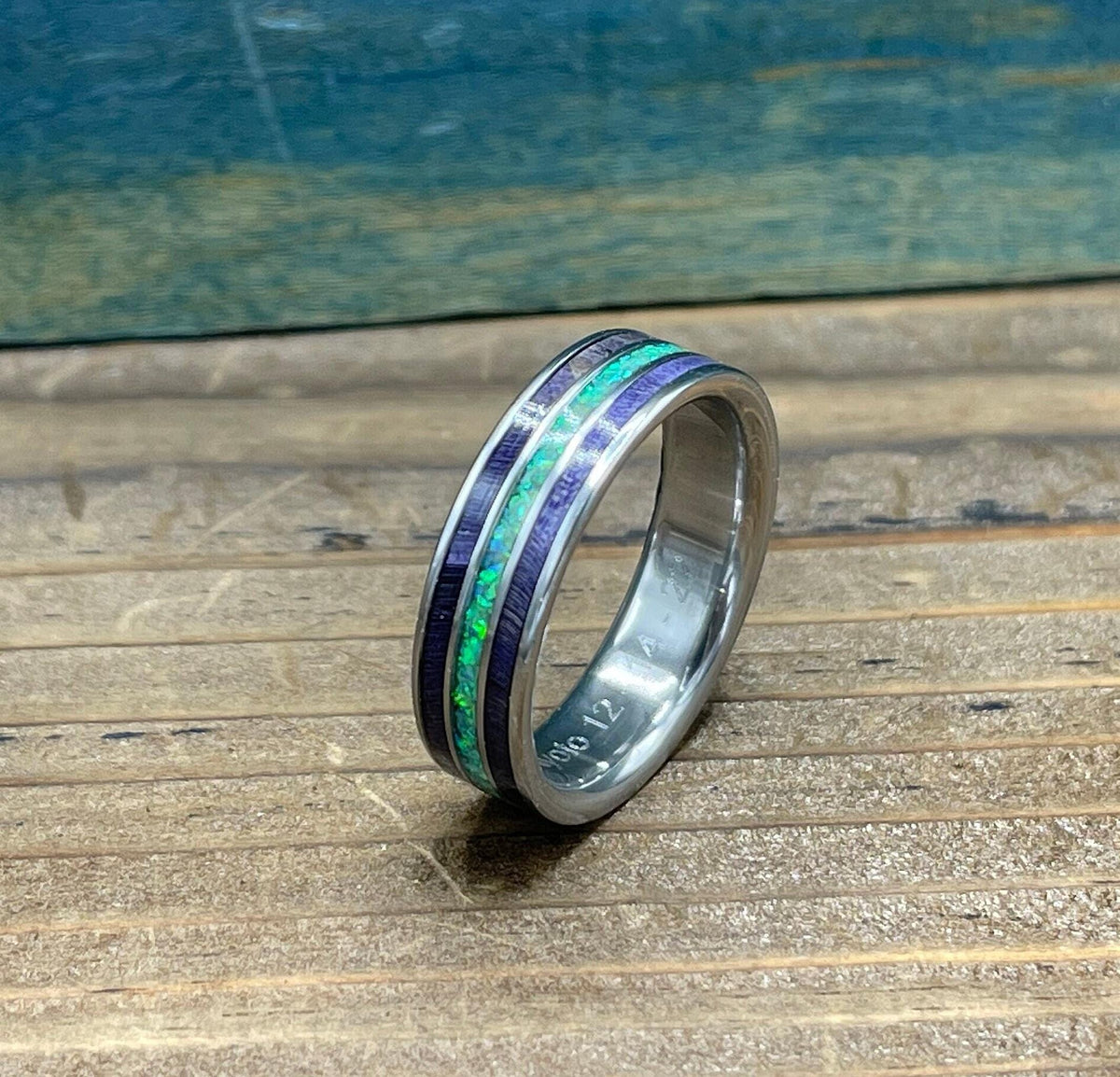 A silver ring with purple wood and green opal inlay is shown from the side, with "OLO 12" engraved on the inside band.