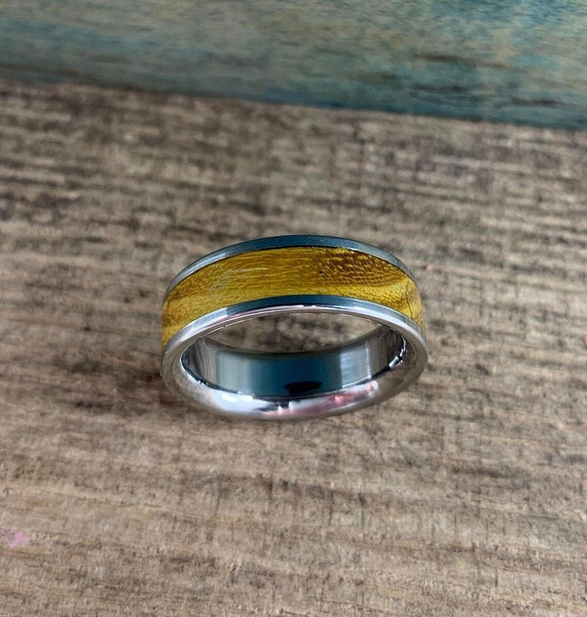 A silver-colored ring with a golden-brown wood inlay is shown from a slightly elevated perspective, with the ring's interior visible.