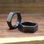 Two dark gray hexagonal rings, one standing upright and one lying flat, on a wooden surface.