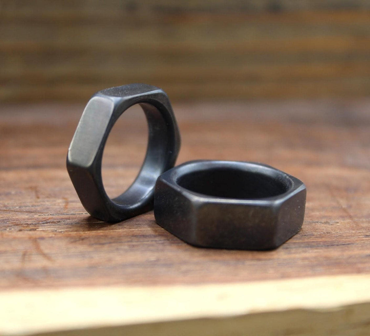 Two dark gray hexagonal rings, one standing upright and one lying flat, on a wooden surface.