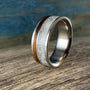 A titanium ring with a central band of white rose quartz and a narrow strip of dark kingwood, shown at an angle on a wooden surface.