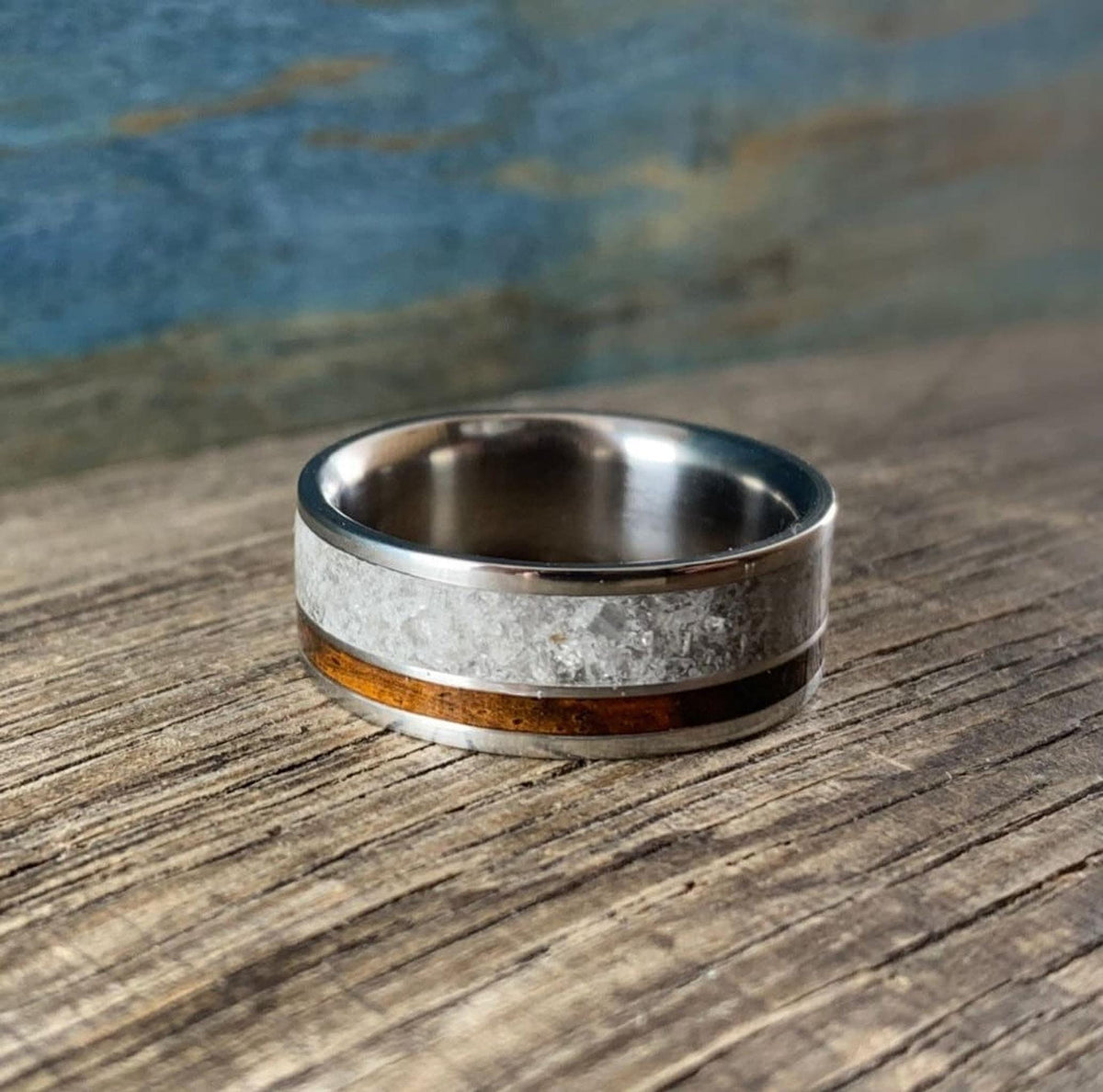 A titanium ring with a wide band of white rose quartz and a narrow strip of dark kingwood, shown from the side on a wooden surface.