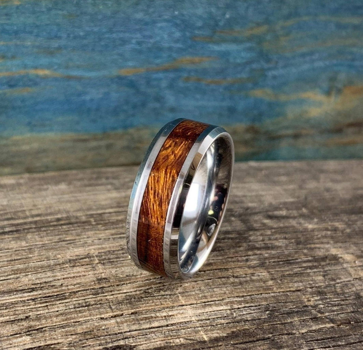 A silver-toned ring with a central ironwood inlay, angled slightly on a wooden surface with a blue and brown background.