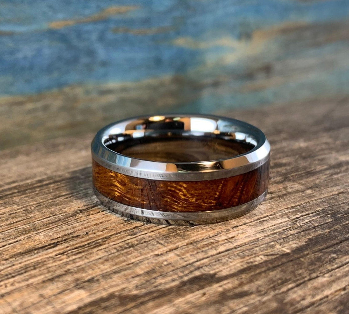 A silver-toned ring with a central ironwood inlay, viewed from the front on a wooden surface with a blue and brown background.