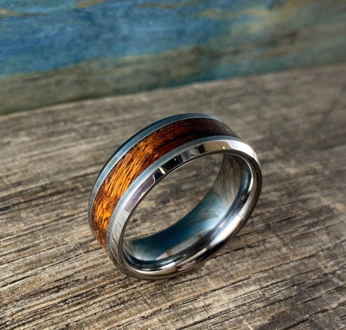 A silver-toned ring with a central ironwood inlay, viewed from a different angle on a wooden surface with a blue and brown background.