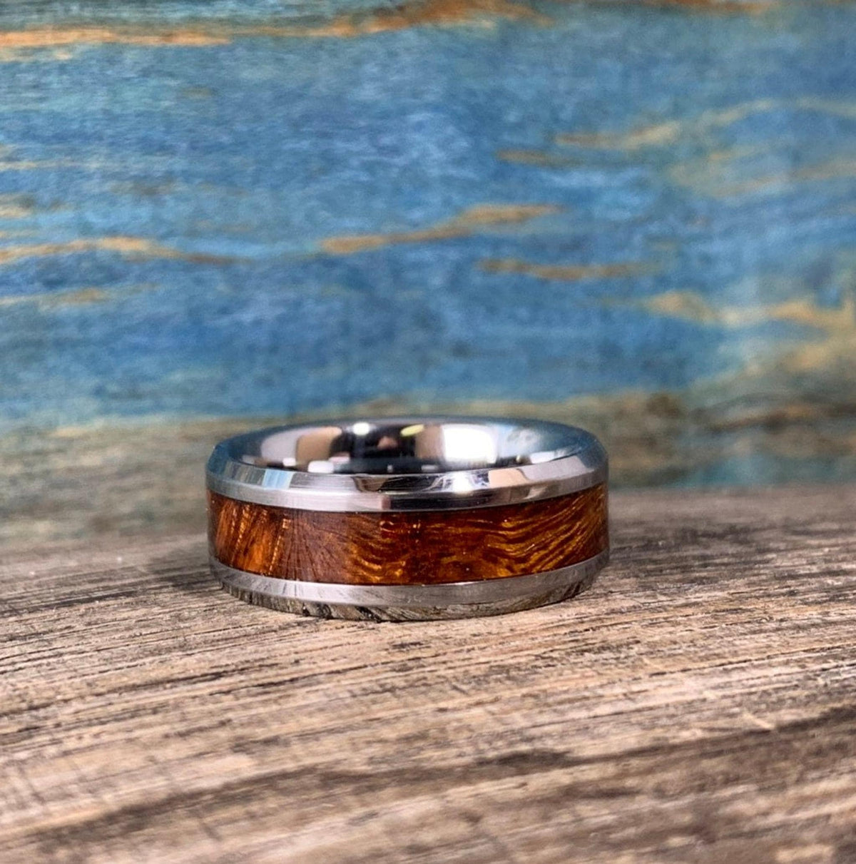 A silver-toned ring with a central ironwood inlay, centered on a wooden surface with a blue and brown background.