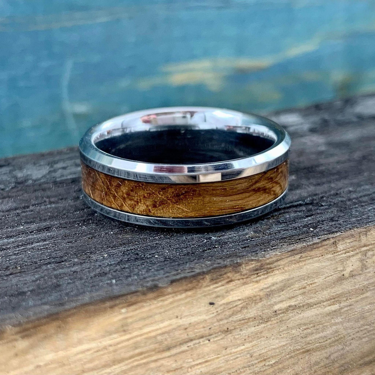 A silver-colored ring with a light brown wood inlay, on a dark wooden surface.