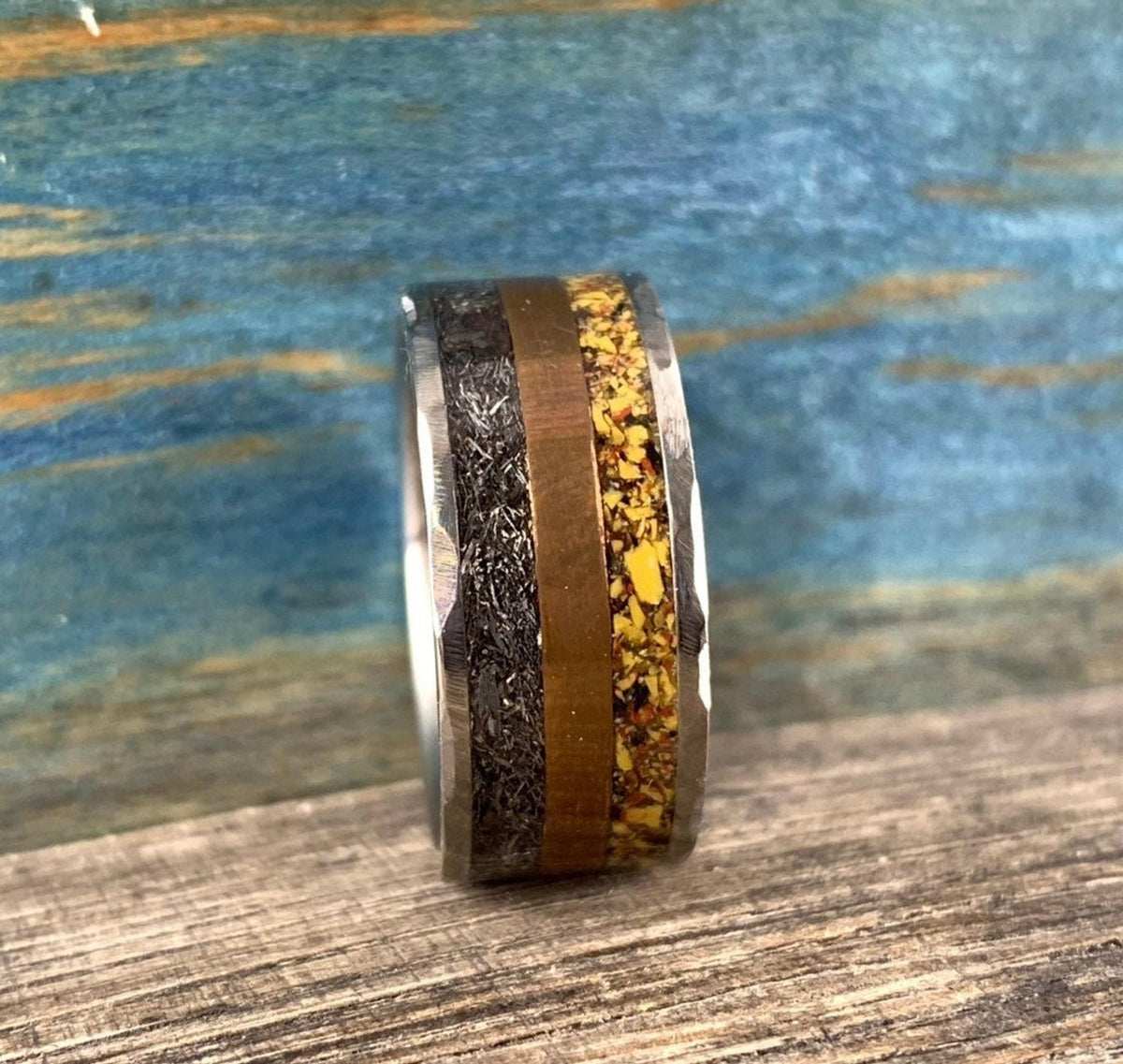 A silver-colored ring with hammered outer edges, a smooth copper-colored band, and a textured yellow-orange band in the center, viewed slightly from above.