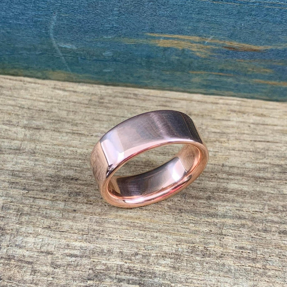 A shiny rose gold-colored ring with a slightly rounded top surface is angled on a wooden surface.
