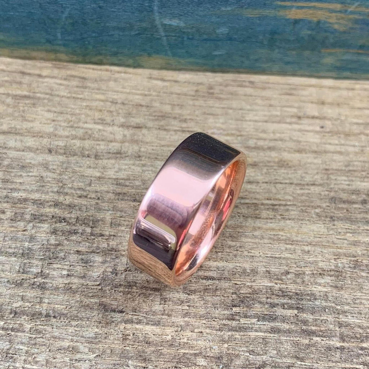 A shiny rose gold-colored ring with a flat top surface is angled on a wooden surface.