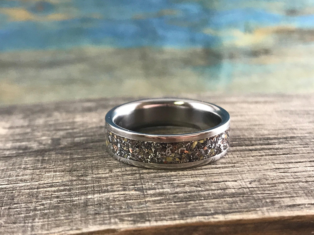 A silver-colored ring with a speckled, multi-colored inlay is centered on a weathered wooden surface.