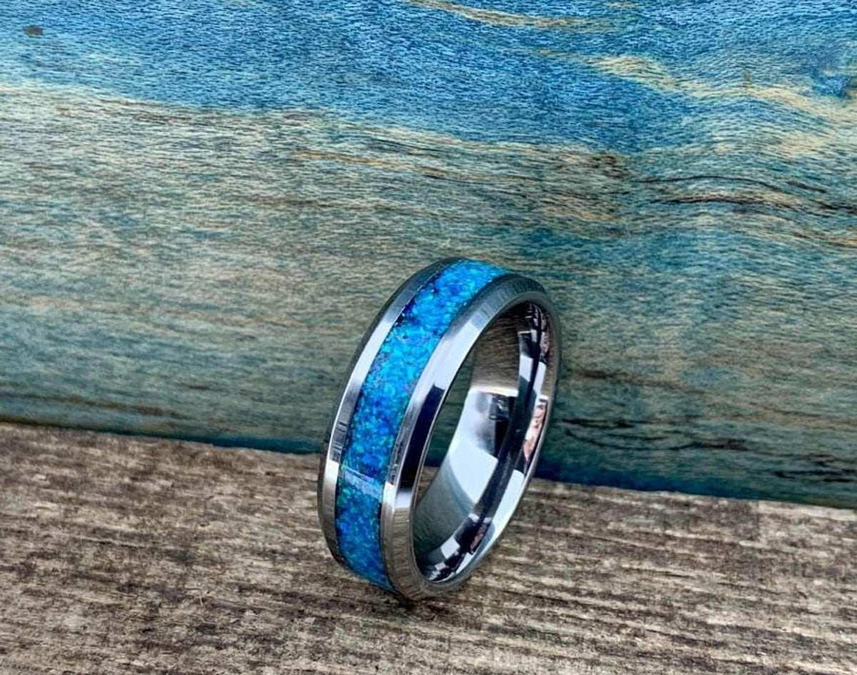 A silver-colored ring with a blue-green opal inlay is centered on a wooden surface with a blue background.