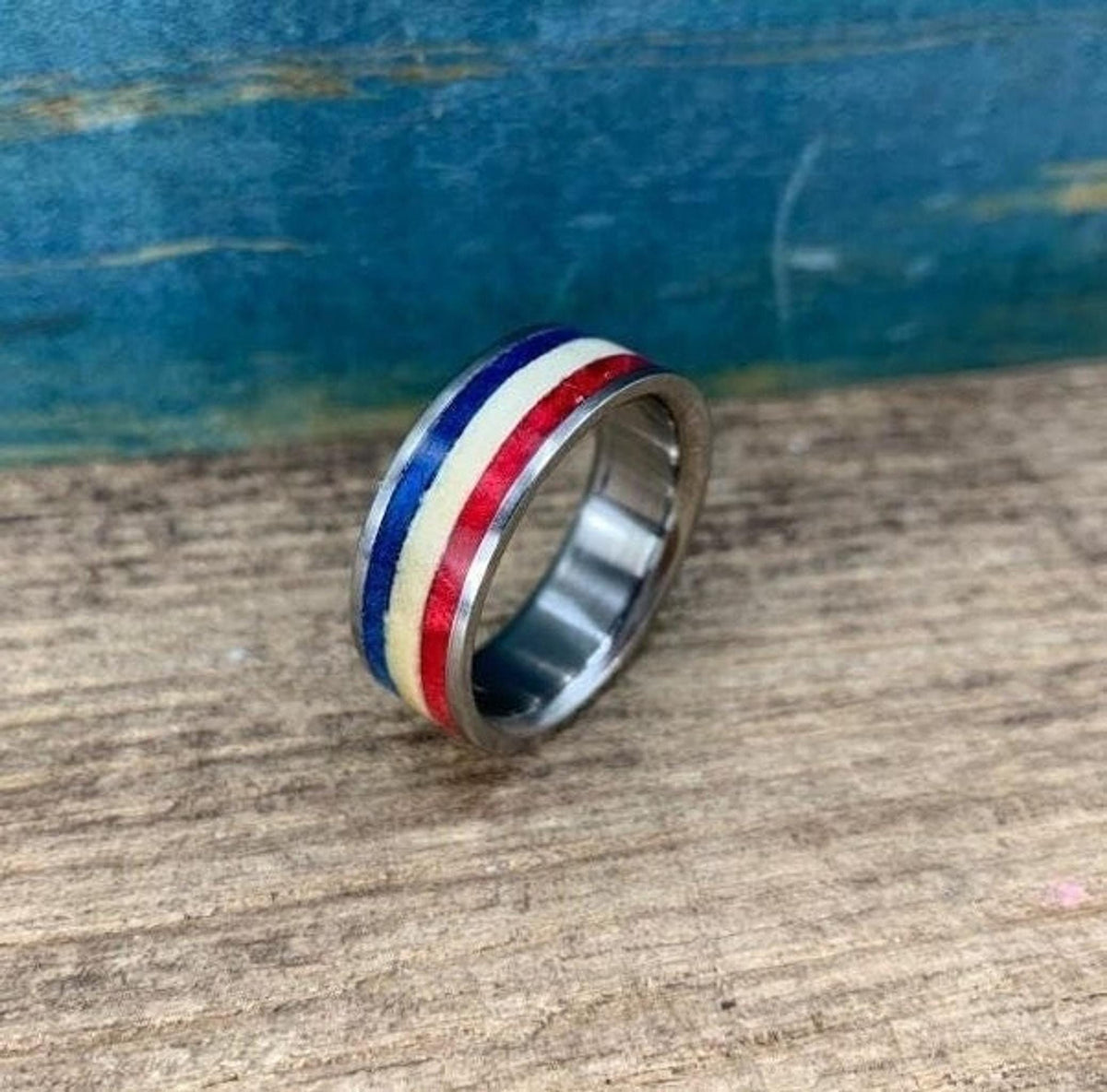 A silver-colored ring with red, white, and blue stripes is angled on a wooden surface.