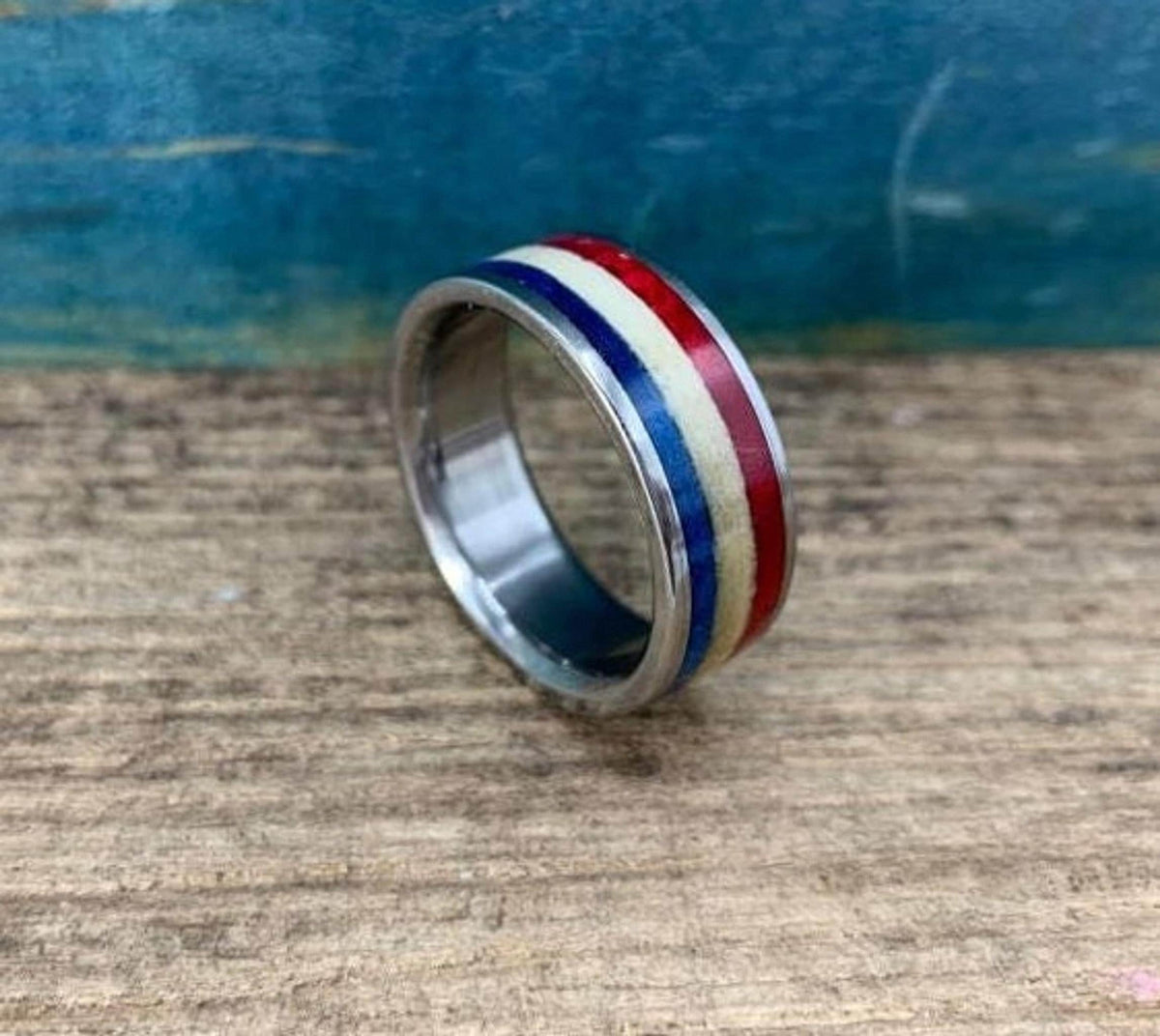 A silver-colored ring with red, white, and blue stripes is shown from a slightly elevated angle on a wooden surface.