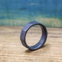 A dark gray, ten-sided ring stands on its edge on a light brown wooden surface, with a blurred blue background.